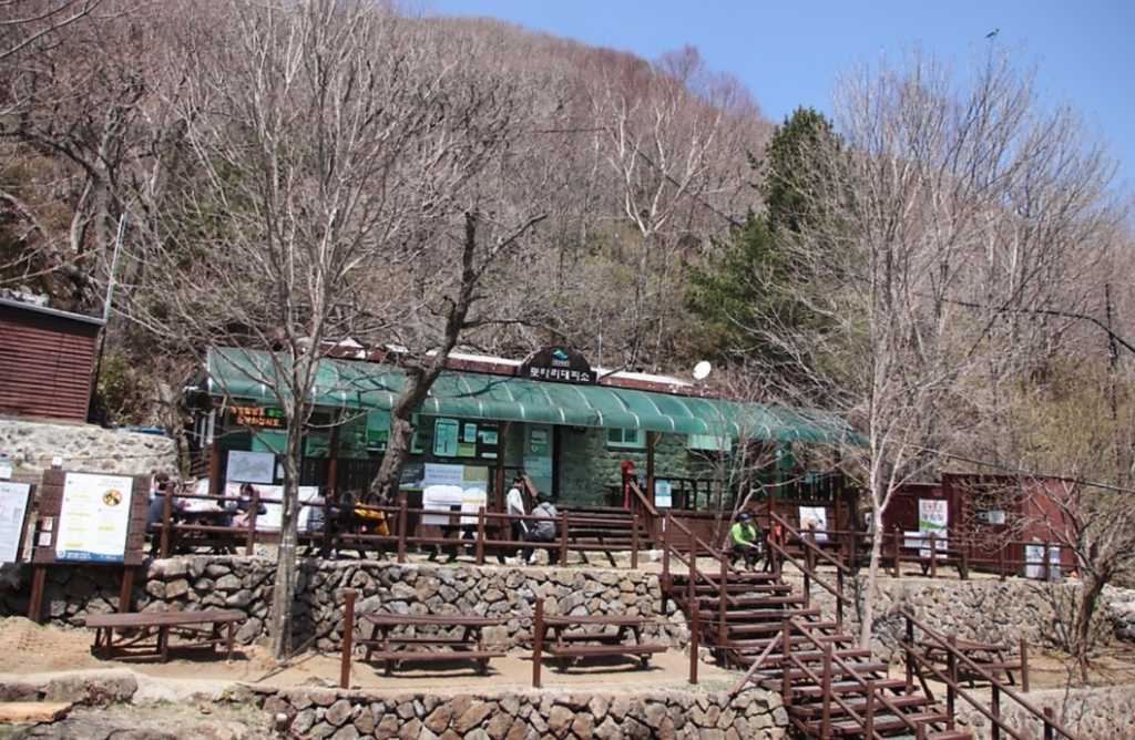The cozy wooden Rotary Shelter located at 1,450m elevation on Jirisan, with hikers resting and enjoying snacks in front of the building.