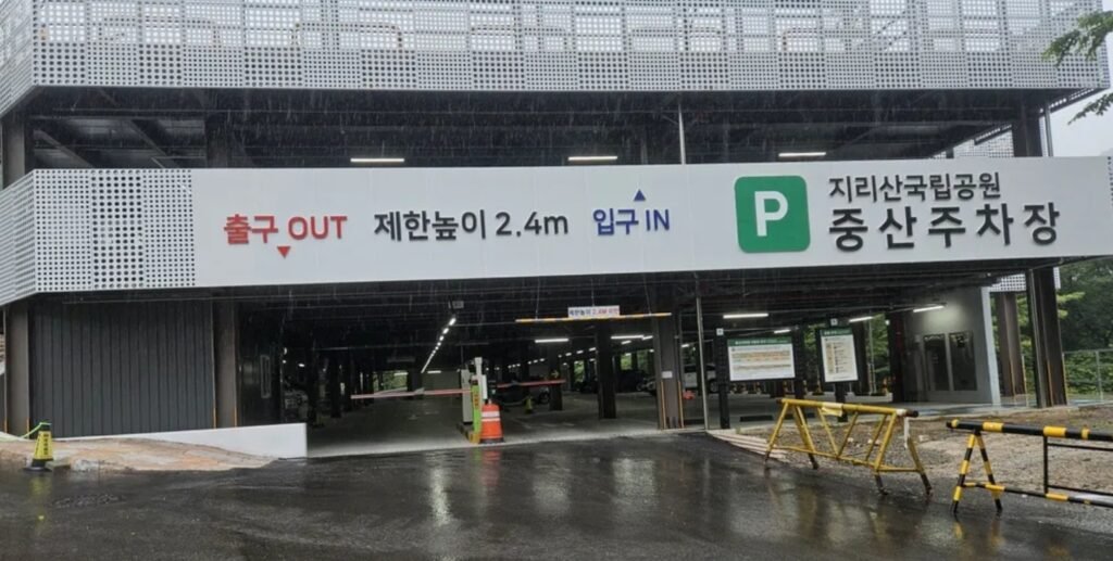 A wide view of the Jungsan-ri branch parking lot at Jirisan National Park, surrounded by lush green trees and featuring ample parking spaces for hikers.