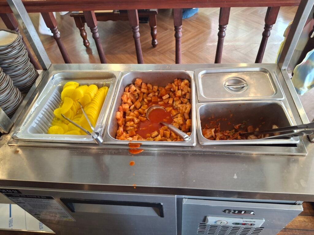 Self-service refill station offering unlimited portions of Kimchi, Kkakdugi, and pickled radish.