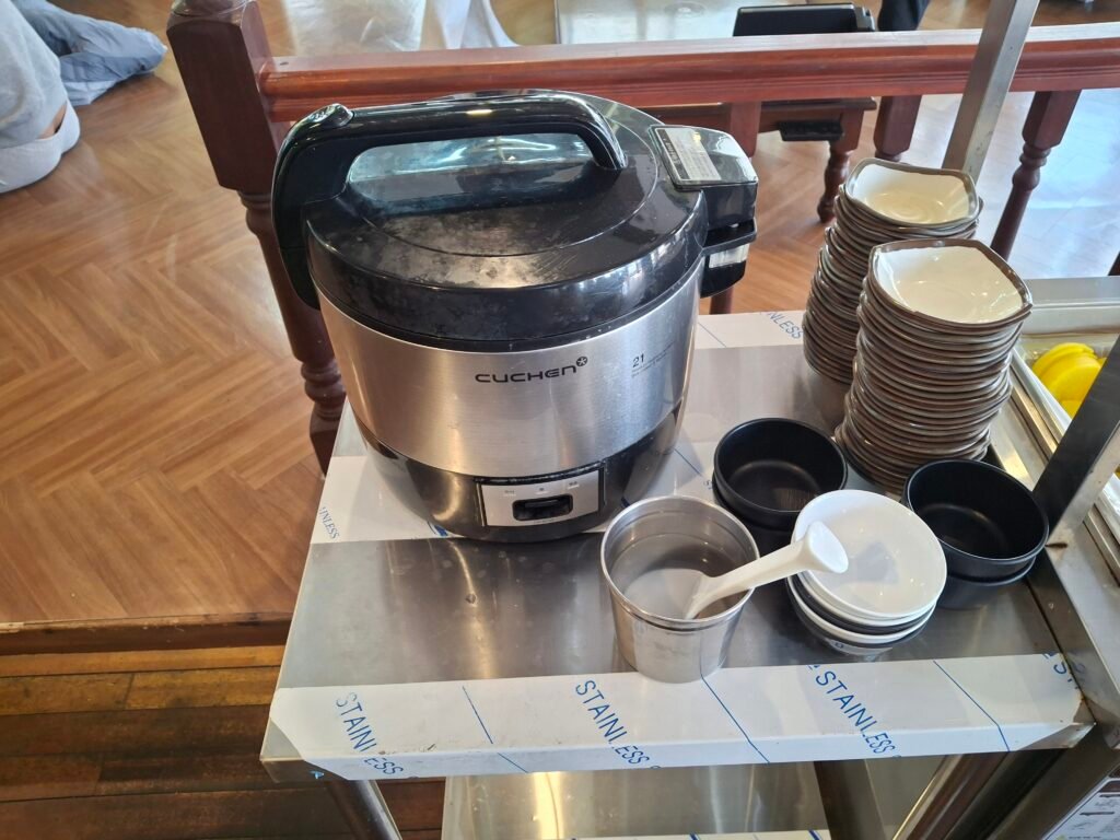 A large rice cooker and bowls at the self-service station offering complimentary rice for guests.