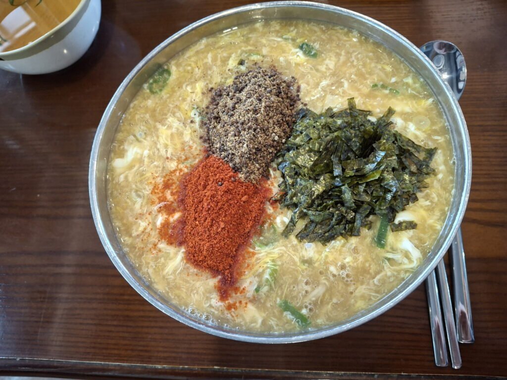 Korean knife-cut noodle soup (Kalguksu) featuring perilla seeds, seaweed, and chili powder toppings on a wooden table