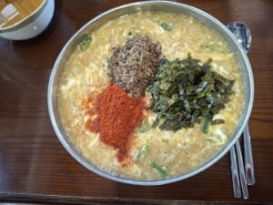 Korean knife-cut noodle soup (Kalguksu) featuring perilla seeds, seaweed, and chili powder toppings on a wooden table