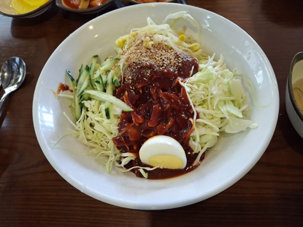 A bowl of spicy Korean chewy noodles (Jjolmyeon) mixed with fresh cabbage, bean sprouts, and sweet gochujang sauce.