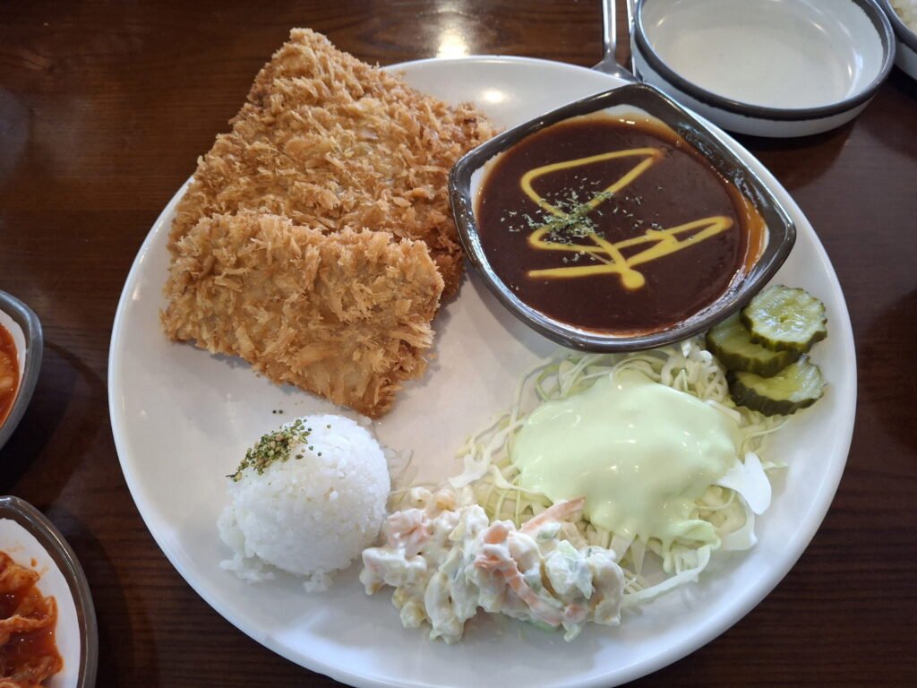 Golden-brown fried pork cutlet (Donkatsu) served with a side of rice, salad, and sauce served separately for extra crunch.